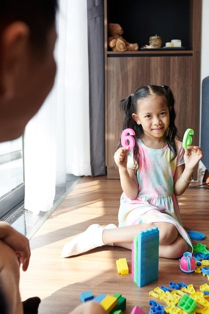A toddler cheerfully placing their toys into a colorful toy bin, with a parent offering gentle guidance and praise. The background features a tidy and inviting playroom.