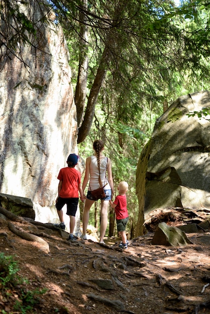 A family hiking a trail in a national park, with towering trees and a clear blue sky in the background. The family consists of parents and two children, all wearing backpacks and hiking boots. They are smiling and pointing towards a distant landmark.