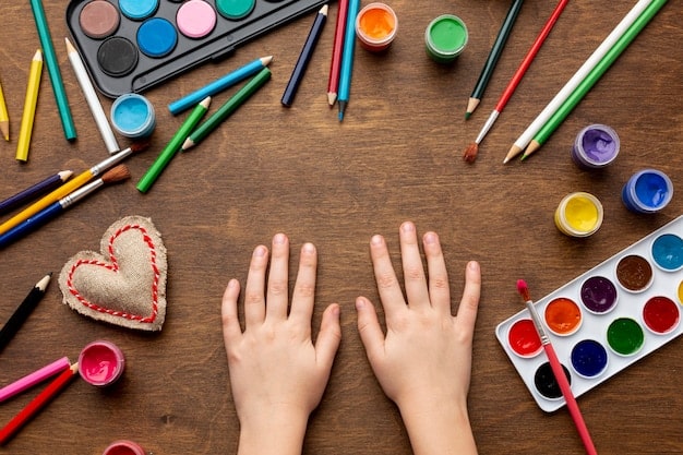 A close-up shot of children's hands painting colorful pictures on paper. Various art supplies are spread out on the table.