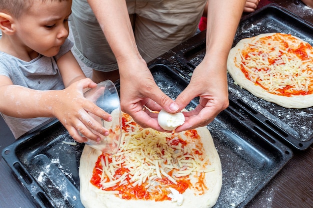 Close-up shot of two young children's hands carefully sprinkling shredded cheese onto mini homemade pizzas. Colorful vegetable toppings are visible, creating a vibrant food scene. Focus on the hands and the pizza, with a blurred kitchen background.
