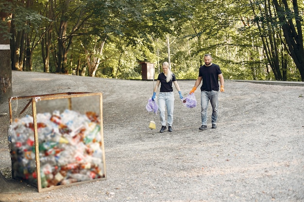 A family is pictured walking through a park, picking up trash with gloves and trash bags. The park is clean and green, with other people enjoying the space in the background. The family is smiling and actively participating.