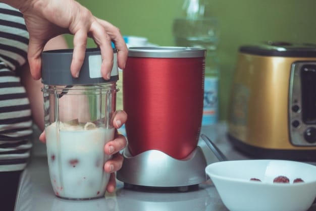 A clear, well-lit image showcasing various types of baby food blenders side-by-side on a kitchen counter. The blenders include an all-in-one steamer blender, an immersion blender with attachments, and a traditional countertop blender, each filled with colorful pureed fruits and vegetables.