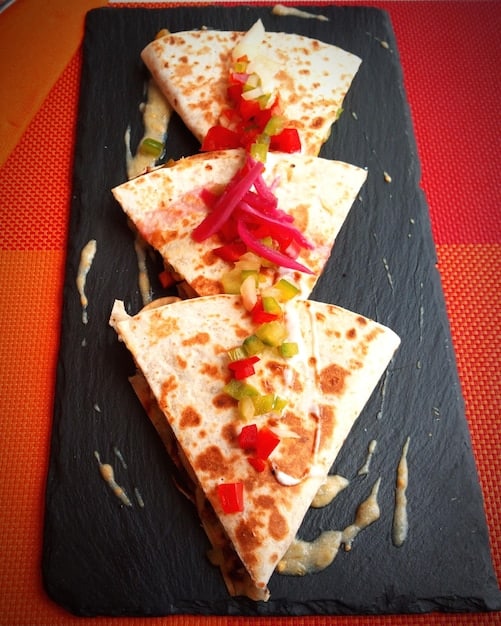 A close-up shot of Sweet Potato & Black Bean Quesadillas cut into triangles, arranged on a colorful plate. The filling is visibly textured, and the tortillas have golden-brown grill marks.