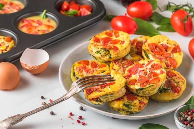 A close-up shot of a tray of colorful egg muffins with various fillings like spinach, cheese, and bell peppers. The muffins are arranged neatly on a baking tray.
