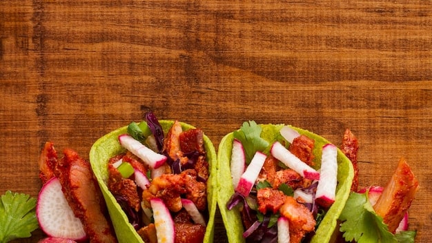 A close-up shot of colorful and appetizing plant-based tacos, filled with a variety of vegetables and topped with a creamy sauce. The tacos are arranged on a wooden cutting board.