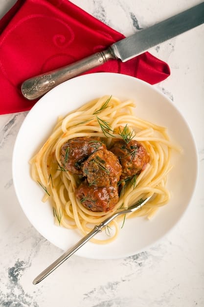 A close-up shot of a plate of spaghetti with meatballs. The spaghetti is covered in a rich, red tomato sauce, and the meatballs are browned and juicy. Finely diced or pureed vegetables (like carrots, zucchini, or spinach) are subtly mixed into the sauce, almost undetectable. The scene emphasizes the hidden veggie content within a visually appealing comfort food.