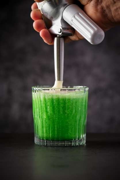 A vibrant green smoothie being poured into a glass. The smoothie contains a mix of fruits and vegetables, like spinach, banana, and mango, blended to a smooth consistency. The focus is on the healthy and appealing nature of the drink, emphasizing the sneaky inclusion of green vegetables.