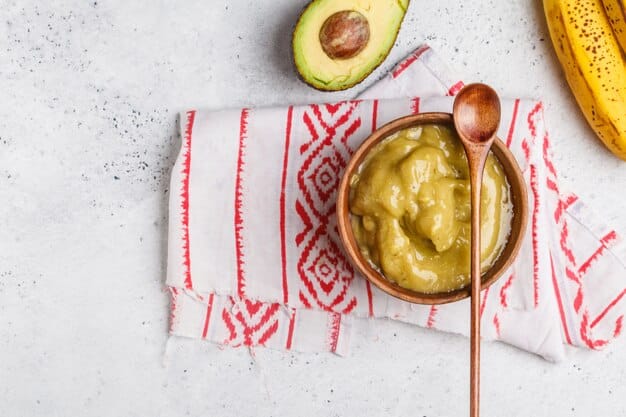 A colorful assortment of single-ingredient purees in small bowls: avocado, banana, sweet potato, and peas. Each bowl is clearly labeled, and the presentation is visually appealing.