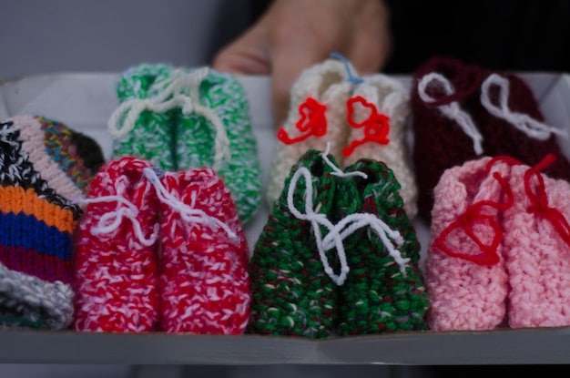 Close-up of a variety of baby carriers displayed on a shelf in a baby store, clearly showing the different styles such as wraps, slings, soft-structured carriers, and framed backpack carriers. The image focuses on the fabric textures and construction details of each carrier type.