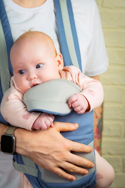 A close-up shot of a baby in a carrier. The baby is positioned correctly, with their hips in an 