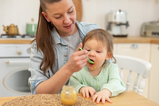 A parent holding a small spoon with a puree of avocado towards a baby's open mouth. The baby is smiling slightly and has a bib on. The focus is on the interaction between parent and baby.