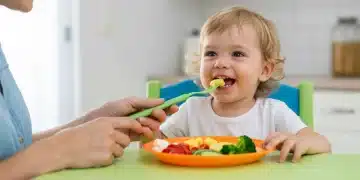 Toddler happily eating colorful healthy food at kitchen table