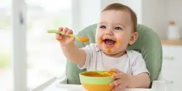Happy 6-month-old baby in high chair reaching for solid food